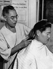 A local newspaper identified Y. Yanagi, shown at work, as the first Japanese American to reopen a barbershop in Little Tokyo following the wartime internment.  The poster in the background promoting National Negro Insurance Week suggests that the shop served African American customers as well as Japanese American ones.